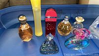 Photo of 7 assorted perfume bottles on blue plastic surface showing brand variety and bottle shapes/colors.