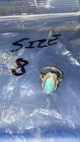 Photo showing a silver ring with oval blue stone on plastic background labeled size 8.