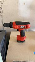 Photo of Black and Decker FireStorm cordless drill 12V showing the red and black drill with attached battery pack on a light wood surface.