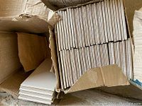 Box containing cream or beige colored ceramic tiles stacked inside.