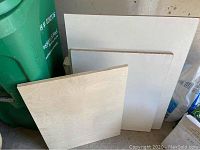 Three plywood sheets of different sizes leaning against a wall, light wood color and smooth finish.