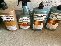 Four bottles of MinnWax hardwood floor cleaning and restoration products on a carpeted surface against a stone wall background