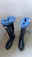 Pair of black tall Hunter original rain boots with grey wool knit socks rolled over the top and inside the boots, size 7.
