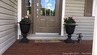 Two black cast iron urn planters placed on porch steps in front of door