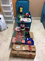 Photo of a large tote filled with assorted holiday decorations, including boxes and loose items on the floor nearby.
