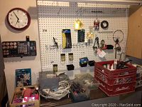 Overview of pegboard with various hanging hardware, wall clock, battery organizer, and tools on counter.