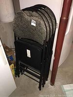 Five black metal frame folding chairs nested together, showing cushioned patterned seats.