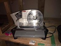 Photo of the full Waring Pro food slicer showing the blade assembly, base, cord, and food carriage on a wooden shelf.