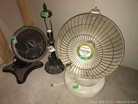 Photo showing the bronze lamp, small black table fan, and Presto HeatDish electric heater together, untested condition visible