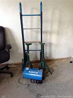 Blue hand cart with two large wheels, two green 5 ton jack stands, and blue Mastercraft gas heater grouped together on concrete floor.