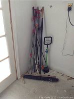 Corner shot showing stacked bar clamps and broom on floor near door.