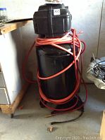 Full view of vertical air compressor with coiled hose and number sticker