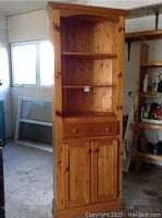 Front view of a tall pine corner cabinet showing open shelving, drawer, and bottom double doors.