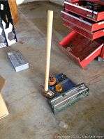 Full view of sledgehammer, hole saw set case with hole saw pieces, and manual tile cutter placed on floor next to tool chest.