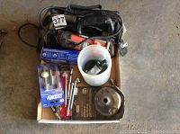 Top view of all tools including Black & Decker rotary saw, small tool bag, grinders, sockets, and accessories on cardboard