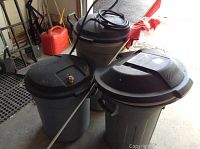 Three garbage cans arranged on garage floor with Canadian flag attached to large wheeled beige can. Shows overall condition and details.