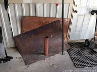 Two copper sheets leaning against wall with a copper coil and two steel rods