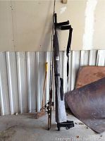 Full view of two fishing rods with reels standing against a wall next to retractable truck bed tarp in gray carrying case.