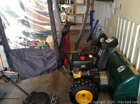 Side profile of green snowblower with vinyl cab in garage