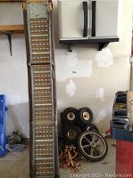 Photo of folding metal ramp alongside miscellaneous tires, rims, and orange straps.