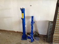 Full view of crane components including upright post and horizontal arm against a wall on a floor with plastic wrap around base.