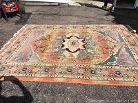 Full view of rectangular rug laid on asphalt showing overall design, colors and fringed ends