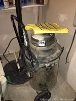 Front view of QSP 8 gallon shop vac showing metal body, black handle, wrapped cord, and yellow papers on top. Visible dirt and wear marks.