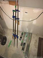 Four bar clamps of different lengths leaning against wall beside several metal drawer slides laid on floor.