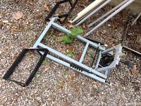 Full view of steel lifting frame with one saddle arm attached, placed on gravel ground.