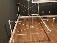 Full view of antique white wrought-iron bed frame showing headboard, footboard, side rails assembled in empty room with wood floor.