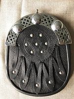 Close-up photo of the black leather Scottish sporran showing the metal top plate with Celtic knot designs and ornamental studs.