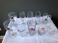 Clear glass beer and brandy glasses arranged on white surface with visible brand logos including Leff, Stella Artois, Hoegaarden, Rickards, Caledonia, Great Lakes Brewery, Ararat