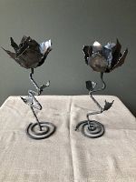 Front view of two iron flower candle holders with twisted stems and spiral bases on beige fabric against dark neutral background.