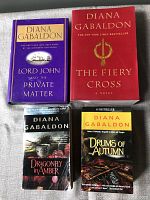 Four Diana Gabaldon books: Lord John and the Private Matter (purple hardcover), The Fiery Cross (red paperback), Dragonfly in Amber and Drums of Autumn (paperbacks)
