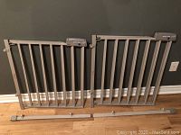 Two Evenflo Secure Step baby gates with grey metal bars and attached extension bars laid out on floor.