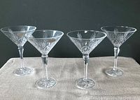 Four 5th Avenue lead crystal martini glasses standing upright, showing the floral etching design on the bowls and starburst pattern on the bases.