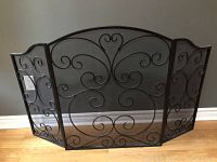 Front view of the black metal fireplace screen with decorative scroll pattern and three panels.