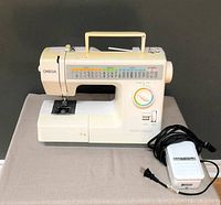 Full view of cream-colored Omega Euro-Delux sewing machine on a table, showing front and side with handle on top and foot pedal beside it.