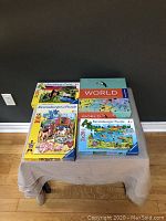 Four Ravensburger puzzle boxes displayed on a small table against a dark background showing colorful children's puzzles, including farm and world scenes.
