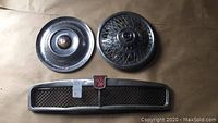 Two different 15-inch hubcaps and MG grill laid out on a surface.
