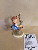 Front view of the M.J. Hummel Apple Tree Girl figurine sitting among apple blossoms on a round white base.