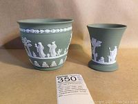 Two-piece set of Wedgwood Jasperware in sage green with classical white relief decoration, showing planter pot and cup side by side.