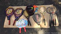 Photo showing main layout of the rackets and paddles including two Prince brand tennis rackets, various sports rackets, and paddleball paddles.