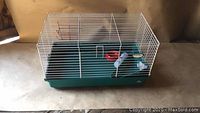 Side angled view of pet cage showing white wire bars and green plastic base with included accessories.