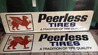 Two horizontal metal Peerless Tires signs stacked showing logos and text