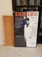 Frontal photo of the Al Pacino Scarface movie poster, 25x39 inches, framed with visible glass, and cork board behind it.
