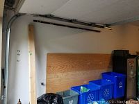 Plywood sheet stored against the wall above recycling bins with visible wood grain and natural wood color.
