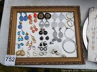 Full assortment of costume jewellery earrings and bracelets displayed inside an ornate gold frame on a white background.