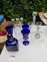 Full lot showing all included items on table: crystal decanter, blue glass vase, Waterford clock, blue stemmed glasses, and clear candlesticks.