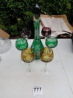 Overall view of the green decanter and six colored wine glasses arranged on table.